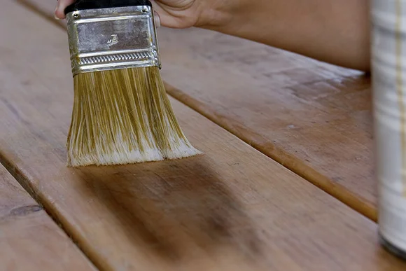 Person streicht Holz mit Pinsel